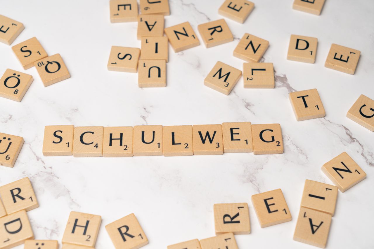 Bainvgnü! Bainvgnüda! Scrabble tiles arranged to spell Schulweg on a white marble surface, creative layout.
